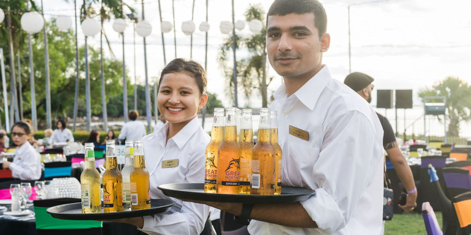 Two servers smiling as they serve beer on trays outside.