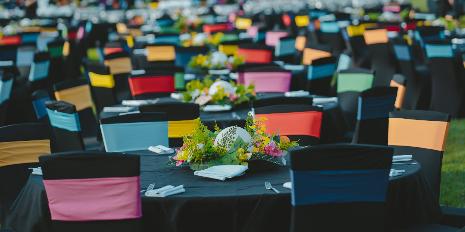 Dozens of tables with flowers and multi colored chairs