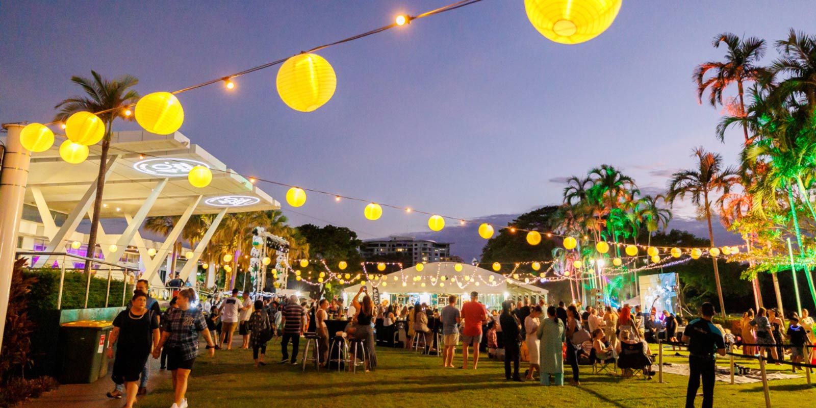 Crowd of people outside at dusk with palm trees and string lights decorating the area