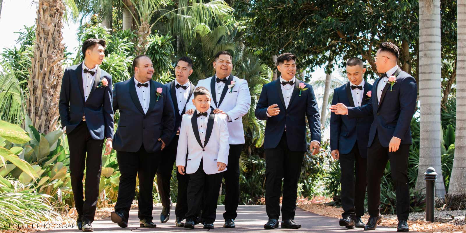 The groom party in tuxes walking outside with palm trees in the background.