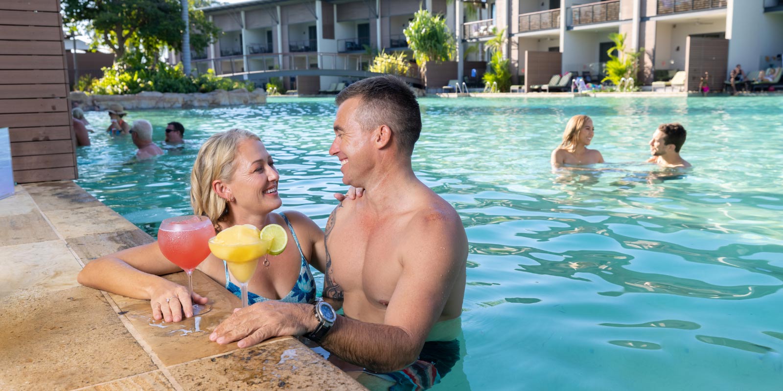 Couple smiling while drinking summer drinks in the pool.