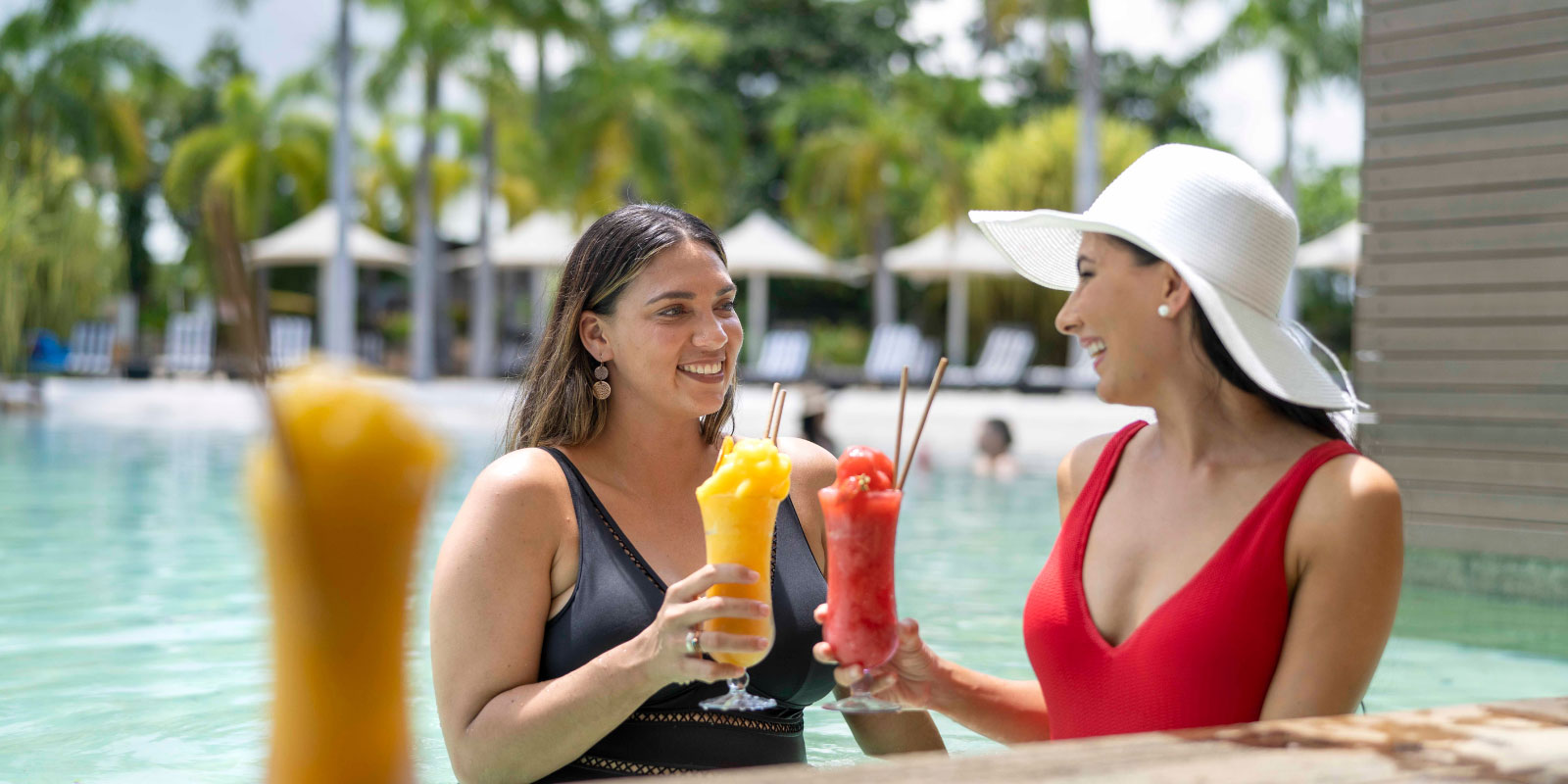 Friends toasting with summer drinks while swimming in the pool.