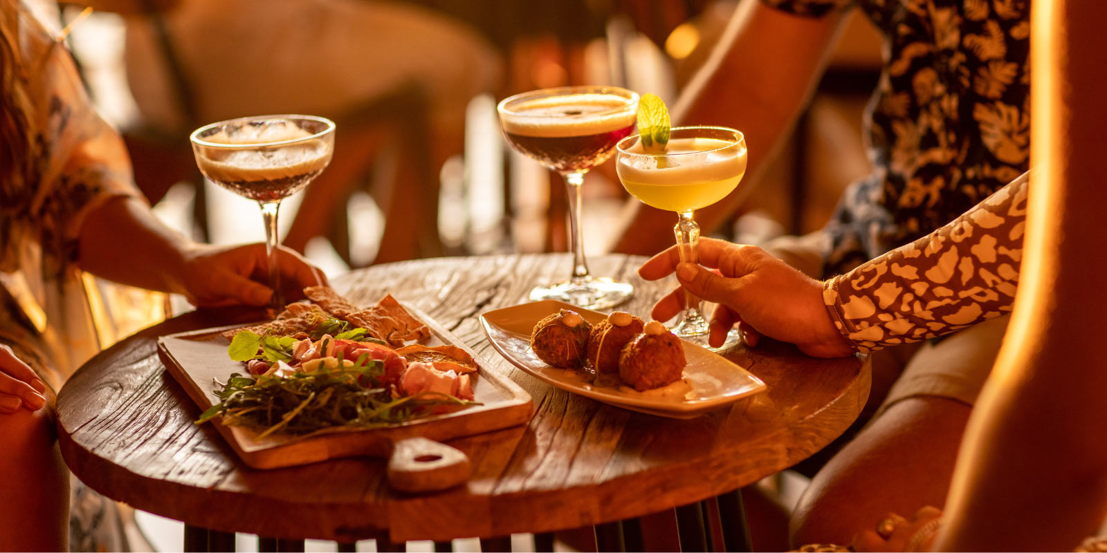 Group of people with drinks sitting at a table with a spread of food.