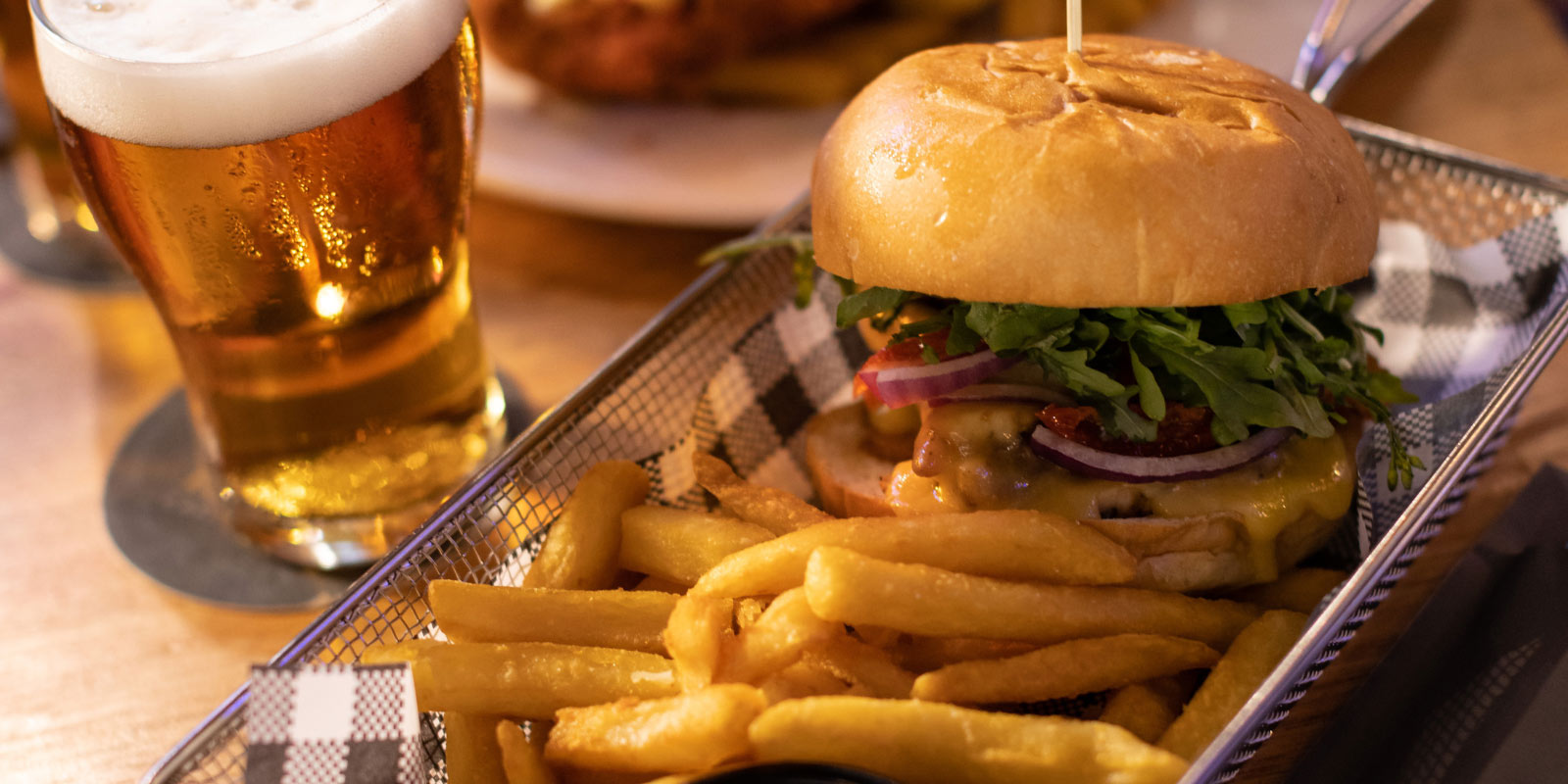 Hamburger and fries in a basket with a pint of beer next to it.