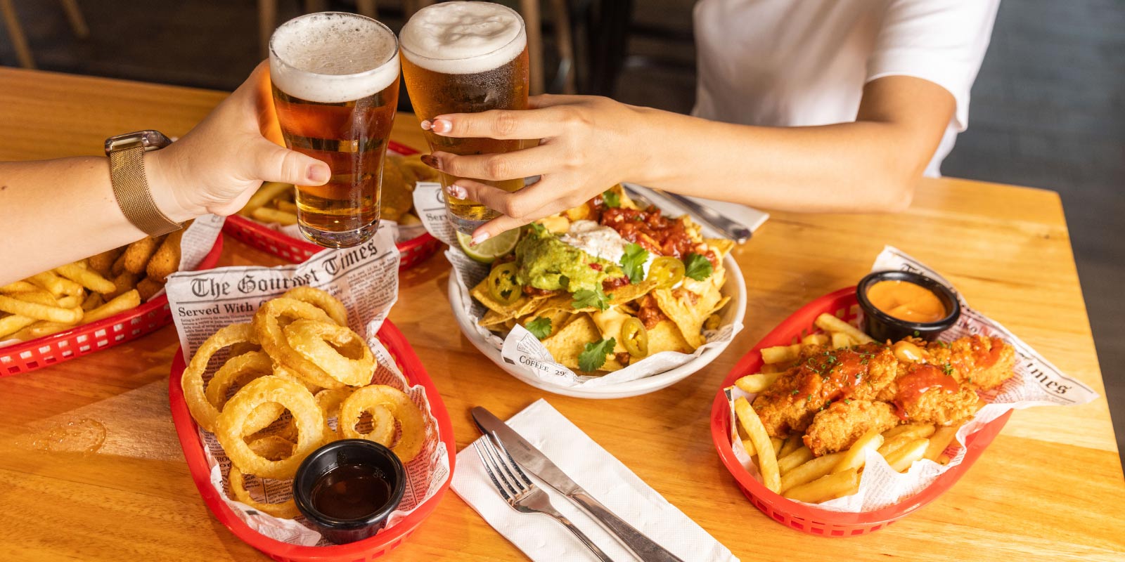 People toasting drinks over baskets of assorted bar food on a table.